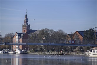 City view with a pedestrian bridge over a river, surrounded by historical architecture and a tower