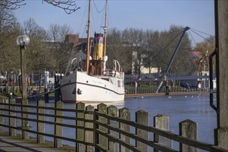 River view with a large boat lying alongside a railing and lanterns, surrounded by trees under a