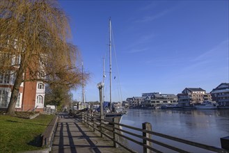 Harbour view with boats and buildings along a waterfront promenade under a clear blue sky in