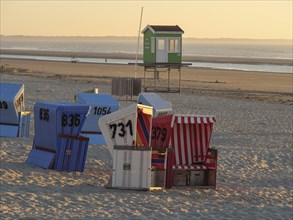 Several colourful beach chairs are scattered on the beach at sunset, with a green guardhouse,