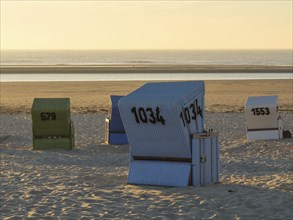 Isolated beach chairs on the beach with calm sea at sunset, langeoog, germany