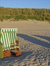 A single beach chair stands on the sunny sandy beach in front of dunes, langeoog, germany