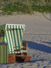 A green beach chair stands on the sand, surrounded by green plants and sunshine, langeoog, germany