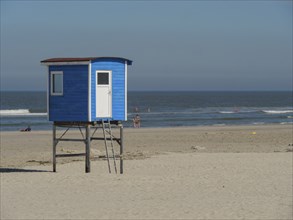 Blue lifeguard tower on sandy beach with calm sea and people in the background, langeoog, germany