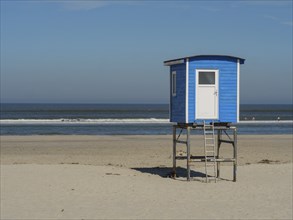 A blue beach hut stands on stilts on the beach near the seashore on a sunny day, langeoog, germany