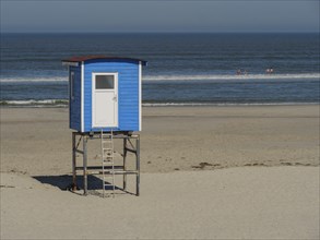 A blue beach hut stands on the beach with the vast sea and sky in the background, langeoog, germany