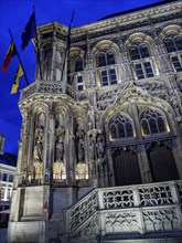 An illuminated Gothic building with flags and sculptures at night, Ghent, Belgium, Europe