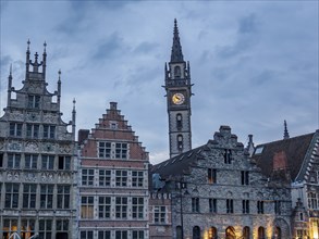 Illuminated historic buildings with a bell tower at dusk under a cloudy sky, Ghent, Belgium, Europe