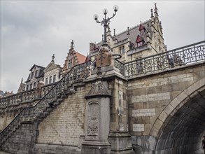 Historic staircase with stone railing leads to a bridge, surrounded by old buildings, under a