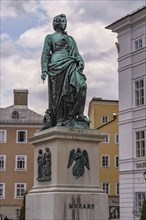 Monument to Mozart on a square surrounded by historic buildings under a cloudy sky, Salzburg,