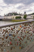 Love locks on a bridge railing with a view of historic buildings along a river, Salzburg, Austria,