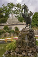 Statue of a rising horse in front of a fountain and historical buildings in the garden, Salzburg,