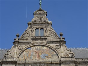 Decorated faÃ§ade of a historic building with religious relief and statue under a blue sky, Ghent,