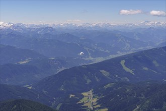 Aerial view of a mountainous landscape with a paraglider in the foreground under a clear sky,