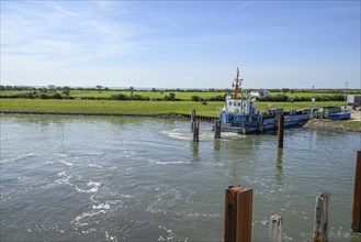 A boat lies on the water, near a quay wall, with green grass in the background and blue sky,