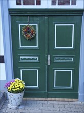 Green double door of a half-timbered house with plant decoration and wreath, Tecklenburg, Germany,