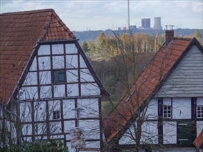 View of half-timbered houses with red roofs and chimneys in a wide landscape with a cloudy sky,