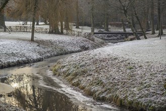 A small stream meanders through a wintry park landscape covered in snow and frost, Velen, North