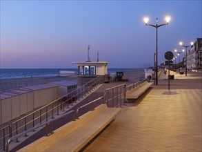 Evening beach promenade with illuminated lanterns and buildings, quiet atmosphere, de haan,