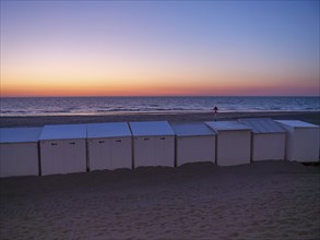 White beach huts at dusk, with an intensely coloured sunset and calm sea, de haan, Belgium, Europe