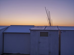 Early sunrise over the sea with white beach huts in the foreground, de haan, Belgium, Europe