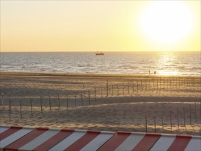 A tranquil scene on the beach with a boat on the horizon and a warm sunset, de haan, Belgium,