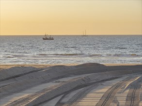 A sunset over the sea with silhouettes of boats and a sandy beach in the foreground, de haan,