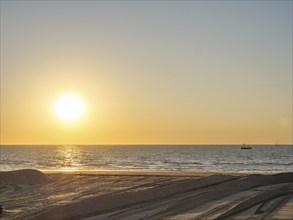 The sun sets over the sea, a boat can be seen in the distance, the atmosphere is calm and peaceful,