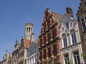 A historic street with stately brick buildings and a large tower in the background, Bruges,
