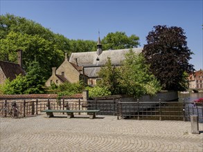 A public square with benches and a historic church building surrounded by trees, Bruges, Belgium,