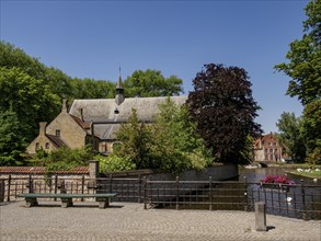 Picturesque parkland with historic buildings, a canal and bridge, surrounded by trees and flowers,