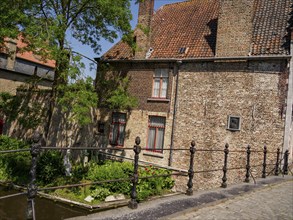 A historic building with a tiled roof and lush green trees along a canal in bright sunshine,