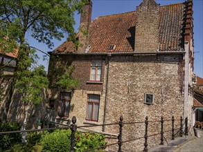 A historic brick building with many windows, surrounded by trees on a sunny day, Bruges, Belgium,