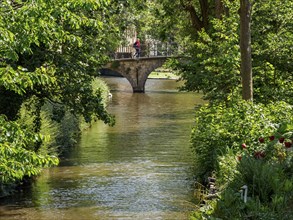 A quiet canal with a stone bridge, surrounded by green trees and plants, Bruges, Belgium, Europe