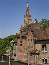 Picturesque scene with a canal, flowers and a bridge against the backdrop of a church tower,