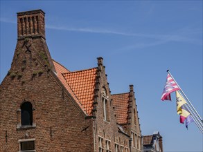 Historic building with tiled roof and flags in Bruges under a blue sky, Bruges, Belgium, Europe