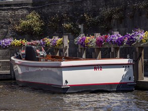 White boat in the harbour, surrounded by colourful flowers and a grey wall, Bruges, Belgium, Europe