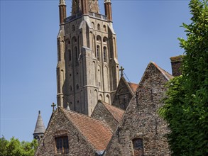 A tall brick church tower next to several historic buildings with Gothic architecture under a blue