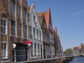 Row of traditional canal-side buildings under a clear blue sky with bridges and road signs, Bruges,