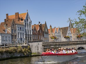 Boat full of passengers travelling along a river, passing historic buildings and a bridge under a