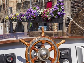 View over the steering wheel of a boat to colourful flowers and historic brick buildings along a