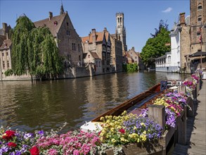 Canal lined with flowers and historic buildings with boats under a clear sky, Bruges, Belgium,