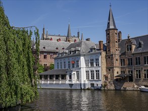 Gothic buildings and church towers reflect in the water under a clear blue sky, Bruges, Belgium,