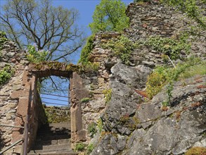 Entrance to a historic ruin with stone walls and an archway, surrounded by green nature and trees,