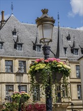 Hanging flower arrangements around an antique street lamp, behind it a historic building with