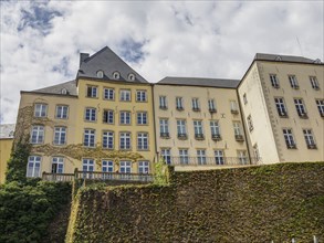 Yellow historic building with many windows and a green exterior wall under a cloudy sky, Luxembourg