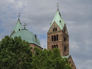 Romanesque cathedral with green roofs and striking towers in the background, surrounded by trees,