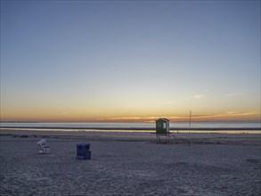 A sunset on the beach with water and clear sky showing a beach hut, langeoog, germany