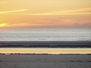 Sunset over the sea with calm water and sandy beach in the foreground, langeoog, germany