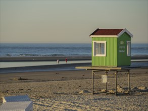 Small green hut on stilts on the beach with sea and people in the background, blue sky, langeoog,